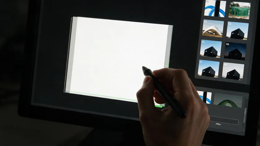A designer using a pen tool on a graphics tablet to manually trace around a subject during photo editing.